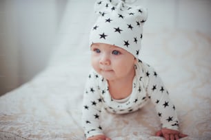 Bebé recién nacido vestido con un traje blanco y estrellas negras es una cama blanca y suave en el estudio.