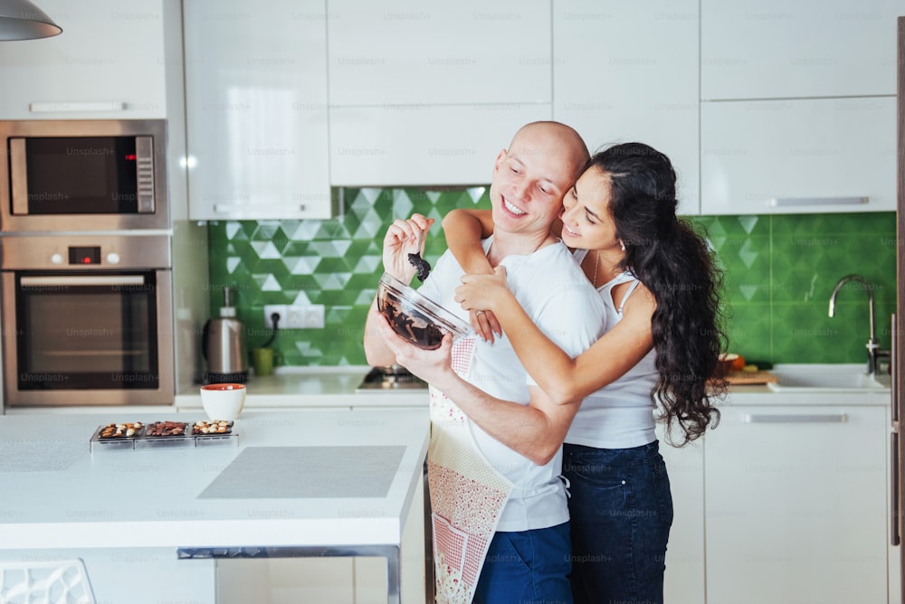 Casal jovem bonito fotografado sorrindo para a câmera enquanto cozinhava na cozinha em casa