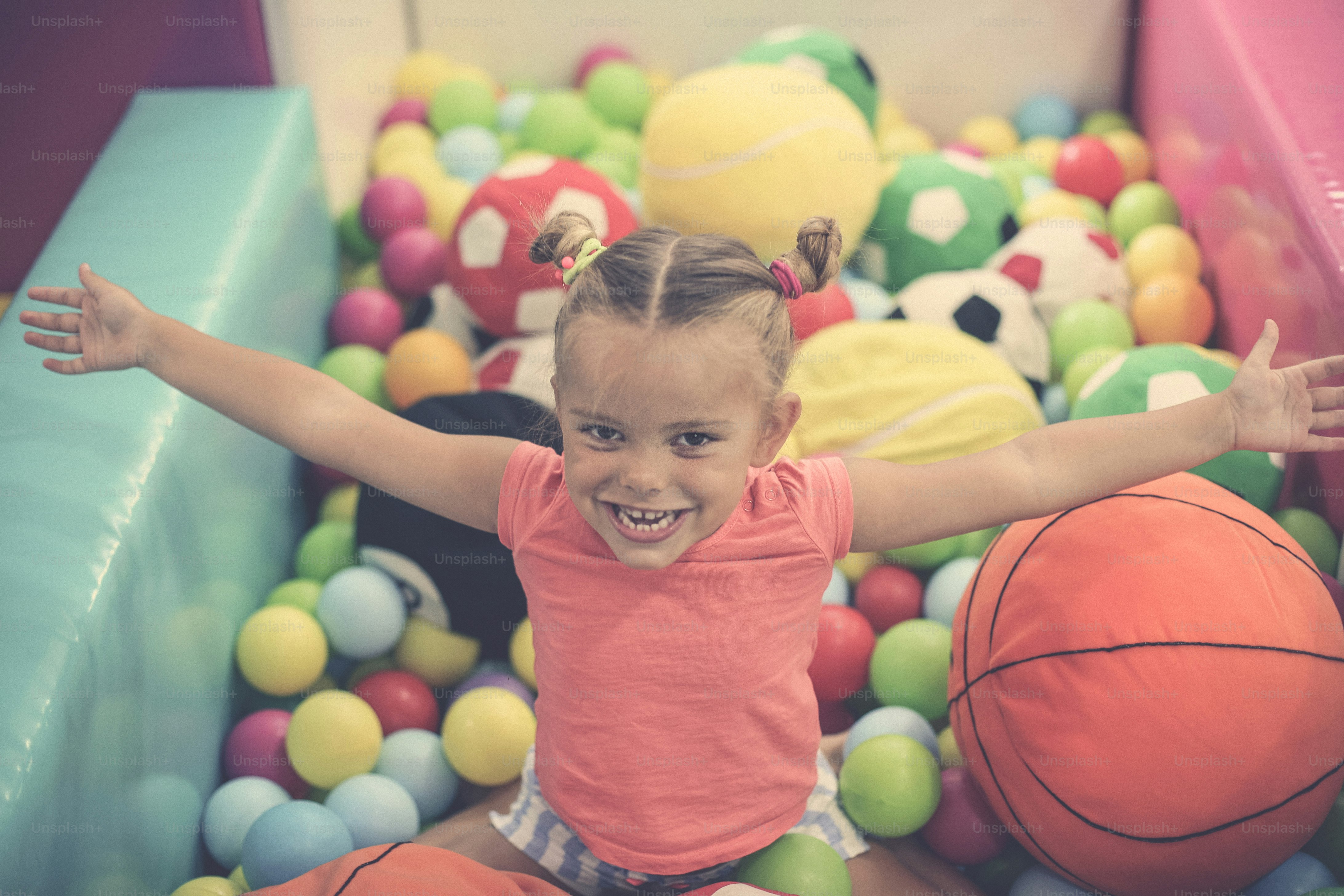 Caucasian girl with open arms sitting on colored ball. Little girl playing in playground.