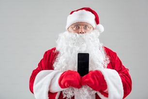 Retrato de cintura para arriba de Santa Claus emocionado mostrando el teléfono inteligente a la cámara. Espacio aislado y de copia