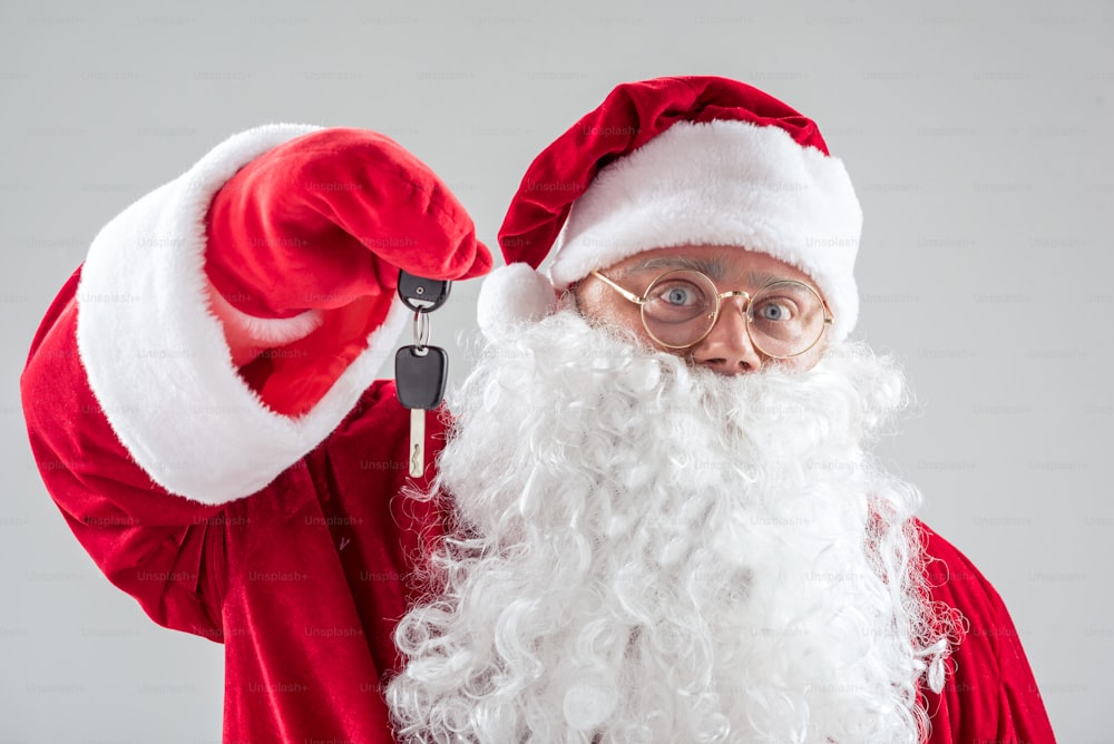 This car is yours now. Portrait of cheerful Santa Claus showing key with joy. Isolated