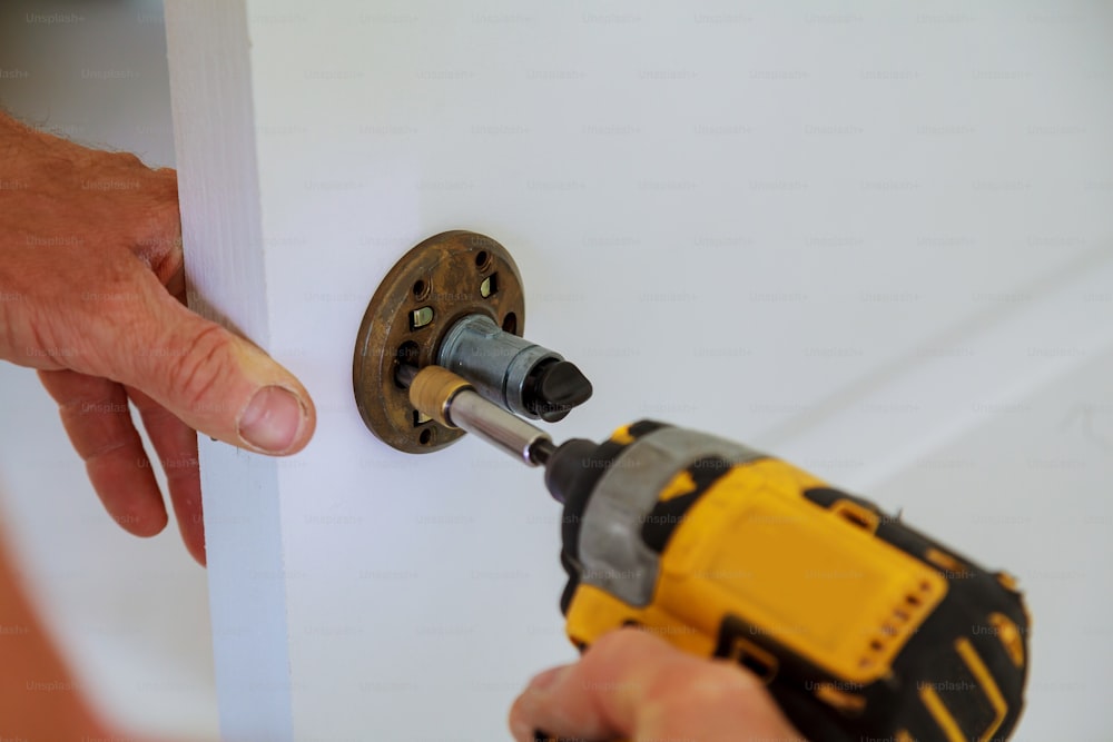 Installation of door lock using a screwdriver to. Carpenter at lock installation with electric drill into wood door. Installation lock. Carpenter installation. electric drill. screwdriver