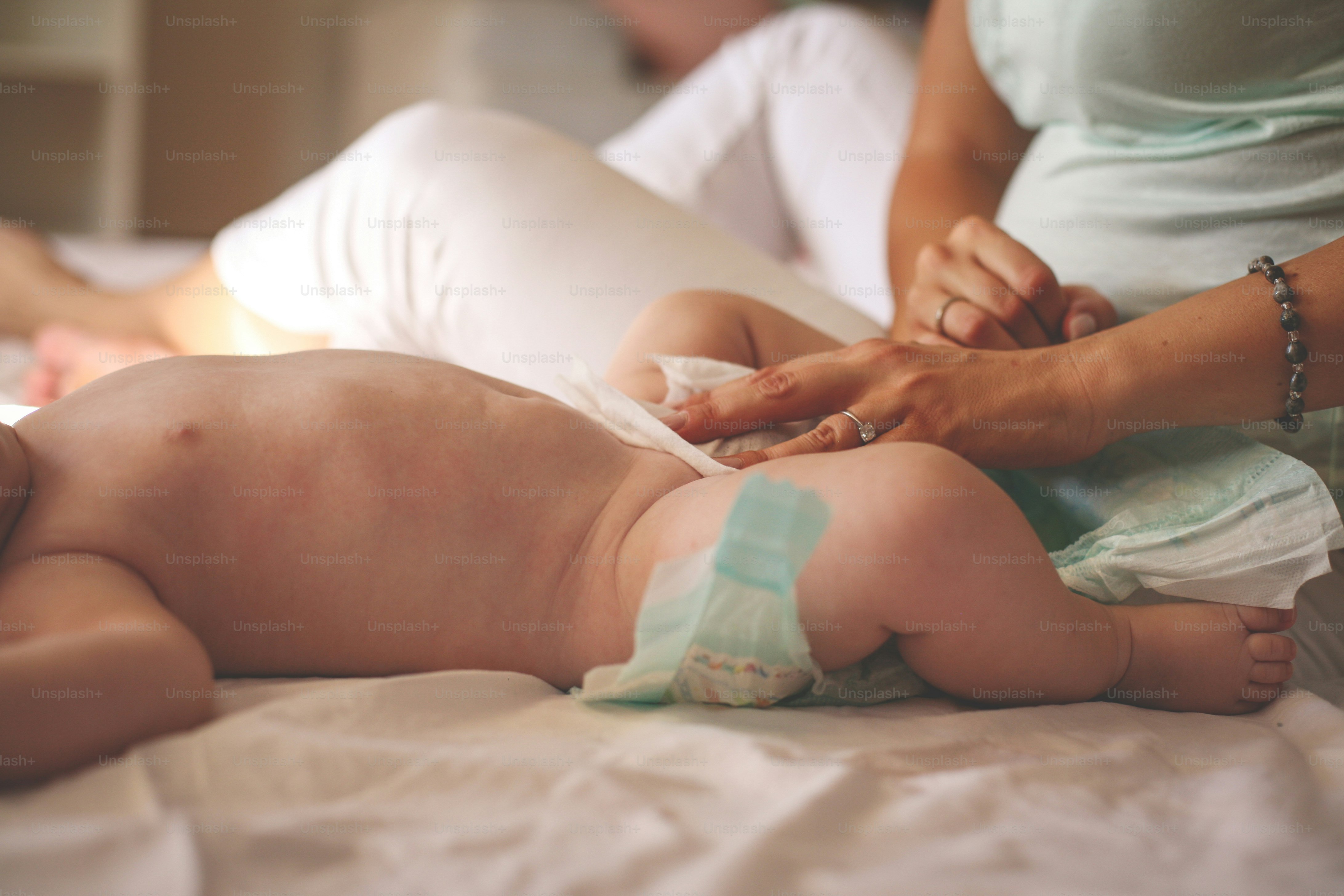 집에서 아기와 함께 있는 어머니. 어머니는 침대에서 어린 아기를 기저귀로 갈아줍니다.