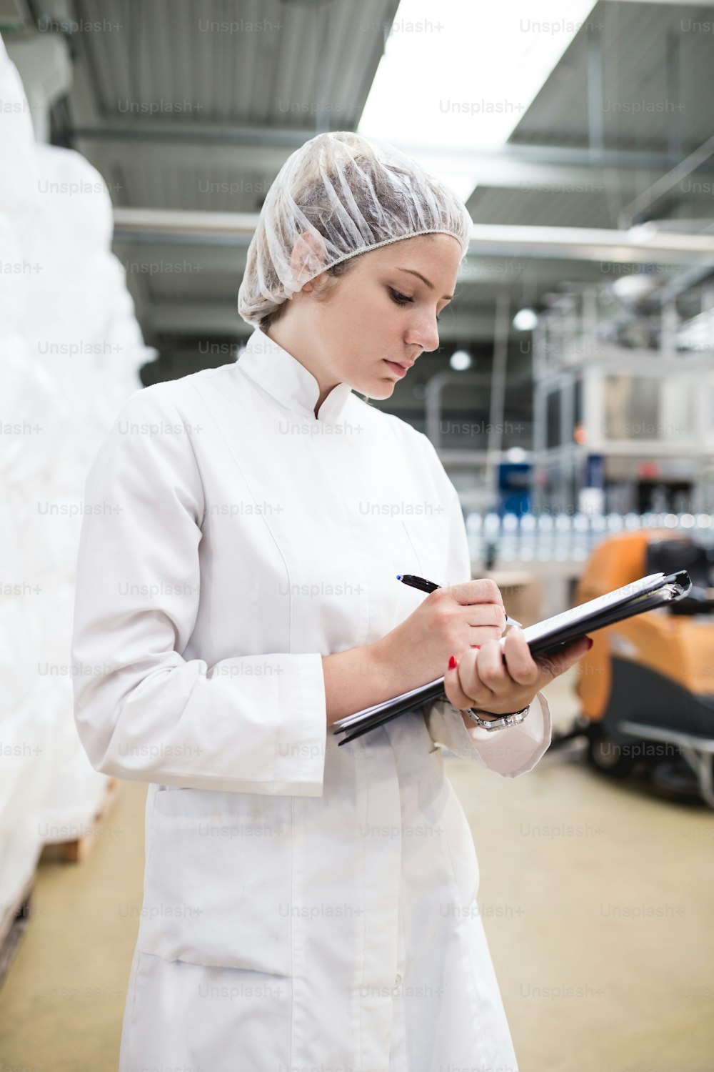 Young happy woman worker checking robotic line for bottling and packaging pure drinking water into bottles and canisters.