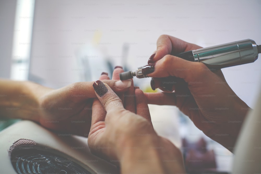 The process of manicure at a beauty salon with electrical  file.  Close up.