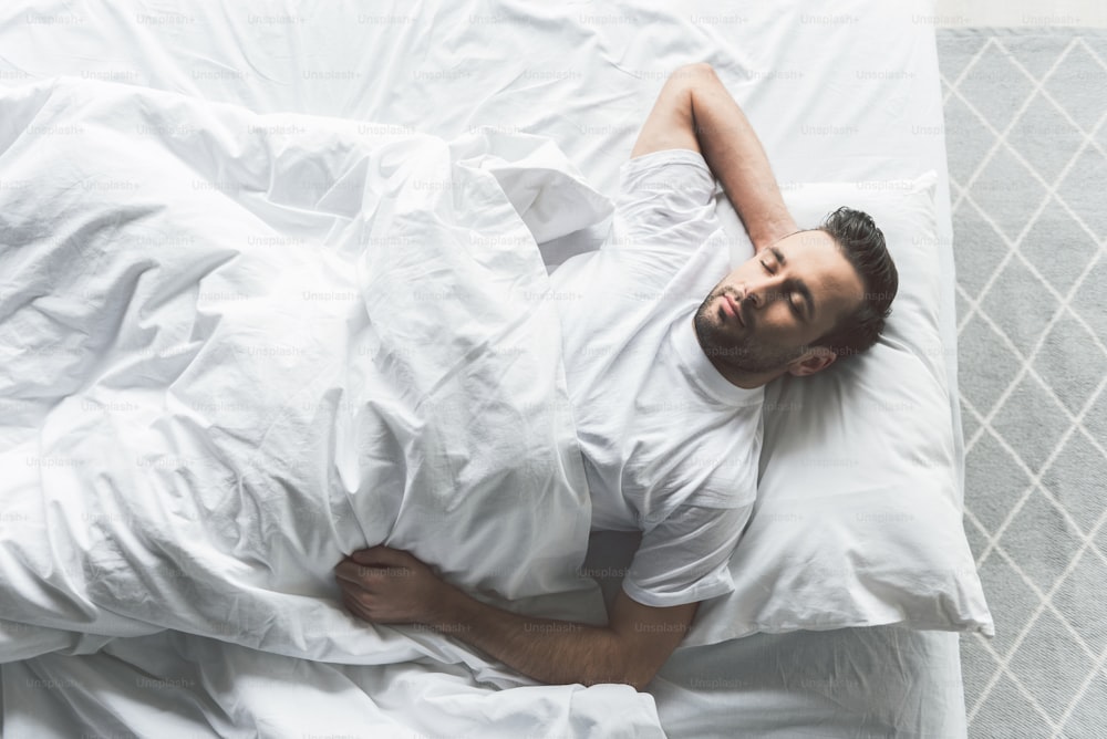Draufsicht auf einen entspannten jungen Mann, der bequem auf dem Bett liegt und schläft. Konzept der häuslichen Harmonie