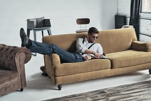 Hübscher junger Mann berührt seine Fotokamera, während er auf dem Sofa liegt