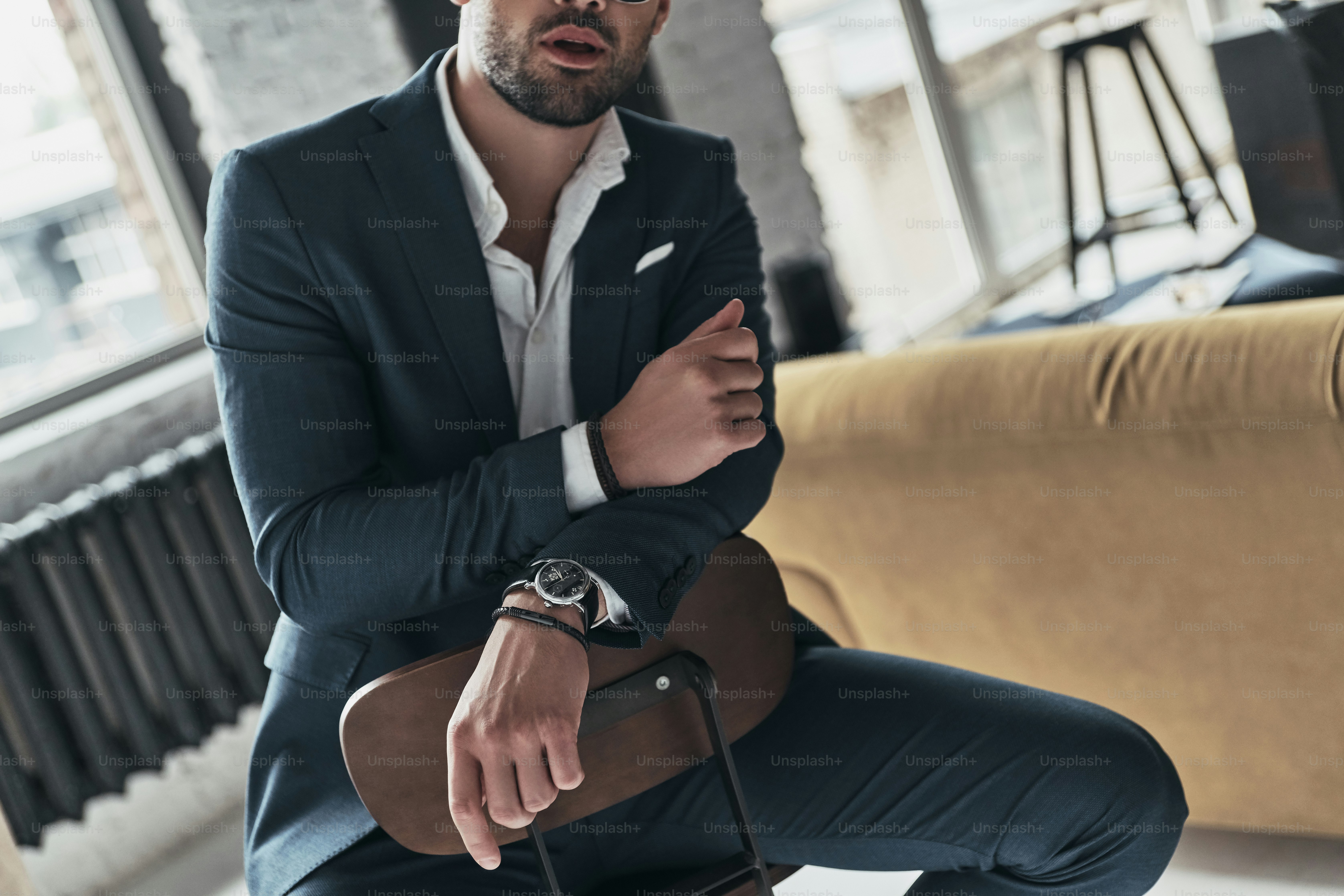 Close-up of young man in full suit sitting on the stool while spending time at home