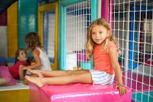 Children in playground. Little girl sitting in playroom and looking away.