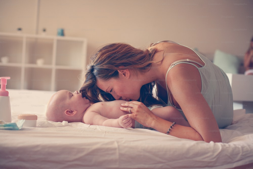 ベッドで男の子と遊んでいる若い母親。小さなかわいい赤ちゃんと自由な時間を楽しむお母さん。