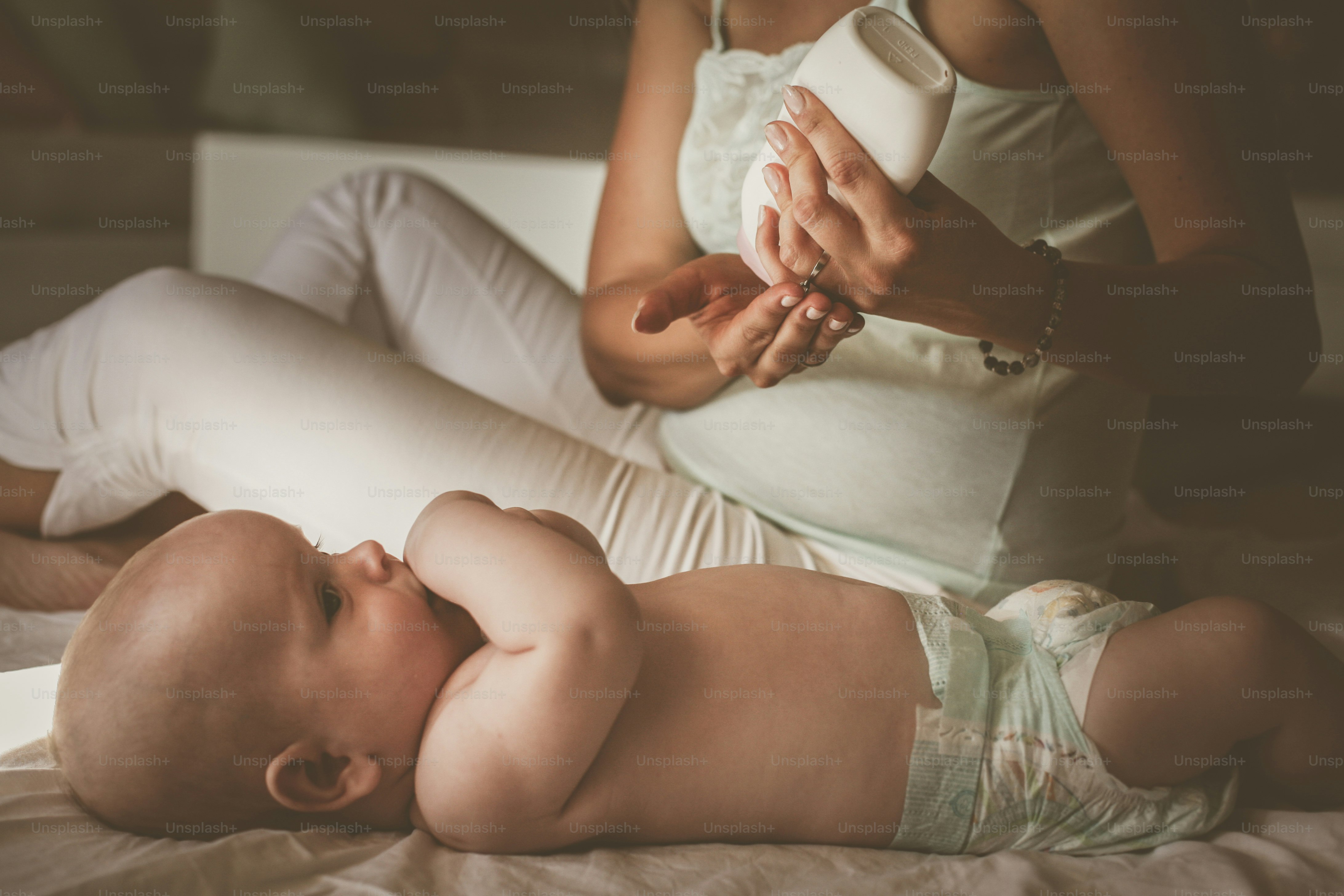 赤ん坊を連れた母親が家にいる。お母さんはボディクリームを使い、赤ちゃんのパッティングをします。