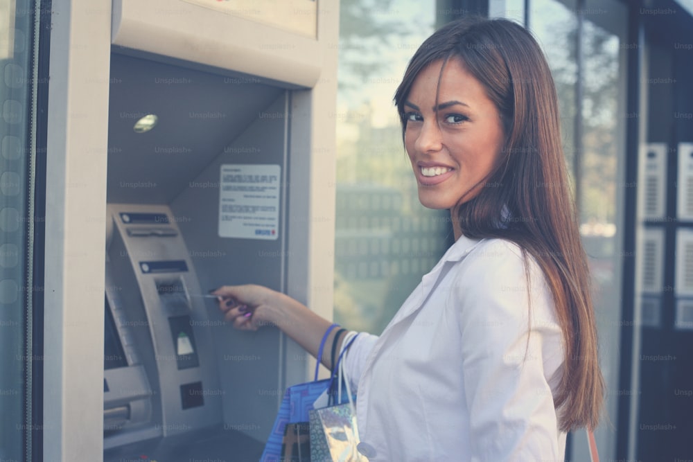 Mujer feliz sonriente con bolsas de compras en el cajero automático. Mirando a la cámara.