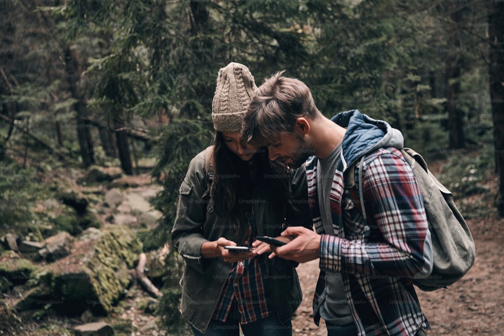 Beautiful young couple using their smart phones while hiking together in the woods