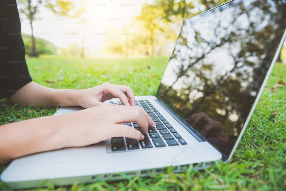 Young asian woman's legs on the green grass with open laptop. Girl's hands on keyboard. Distance learning concept. Happy hipster young asian woman working on laptop in park. Student studying outdoors.