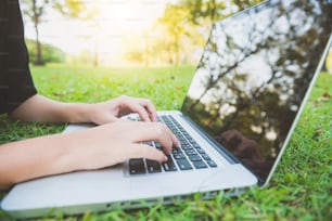 Young asian woman's legs on the green grass with open laptop. Girl's hands on keyboard. Distance learning concept. Happy hipster young asian woman working on laptop in park. Student studying outdoors.