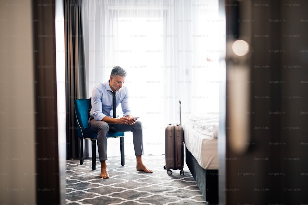 Empresário maduro com um smartphone em um quarto de hotel. Homem bonito enviando mensagens de texto.