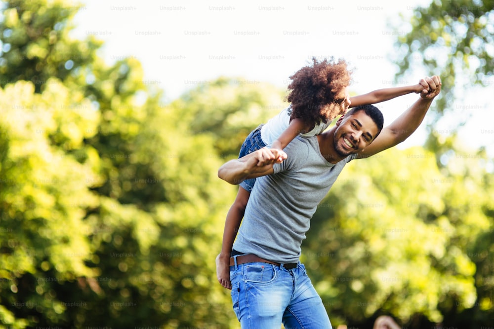 Portrait of young father carrying his daughter on his back in nature