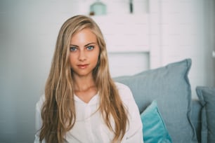 Portrait of a young thoughtful blonde woman sitting in the sofa