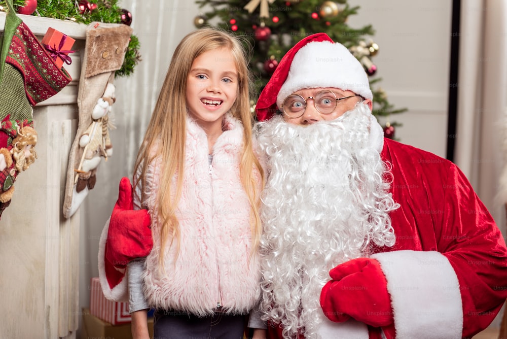 Christmas is my best holiday. Portrait of happy Santa Claus embracing little girl with love. They are standing near fireplace and smiling