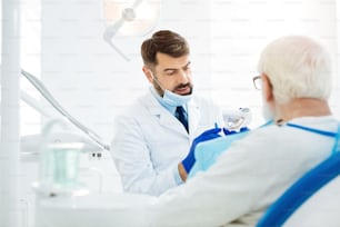 Listening carefully. Attentive experienced stomatologist holding false teeth while demonstrating them to the patient