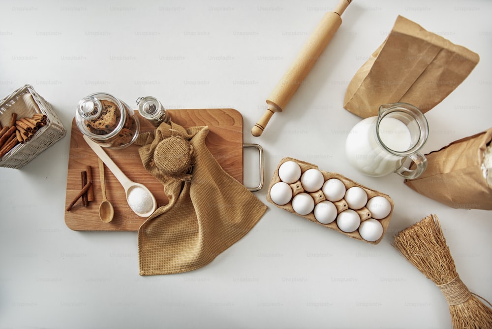 Vista superior de primer plano de huevos, leche y paquete de harina cerca del rodillo en la mesa. Galletas, miel y canela en rama sobre tabla de madera
