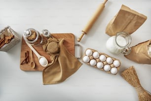 Top view close up of eggs, milk and package of flour near rolling pin on table. Cookies, honey and cinnamon sticks on wood board