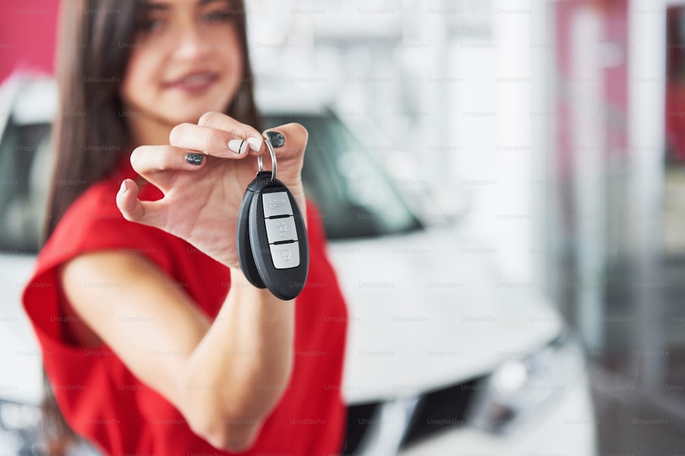 Vendedor de carros sorridente entregando suas chaves de carro novo, concessionária e conceito de vendas. Menina feliz o comprador.