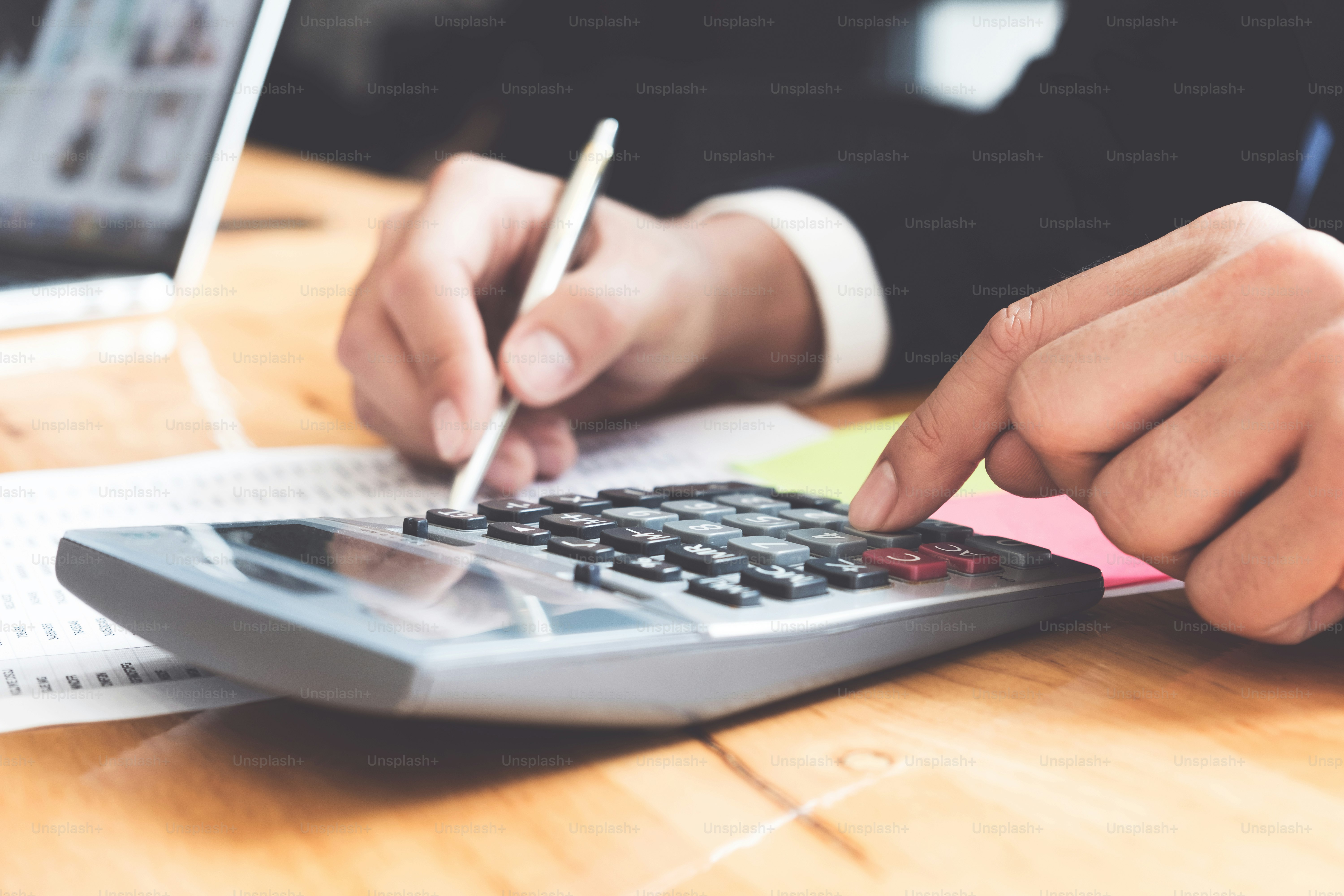 Photo of hands holding pen and pressing calculator buttons over documents