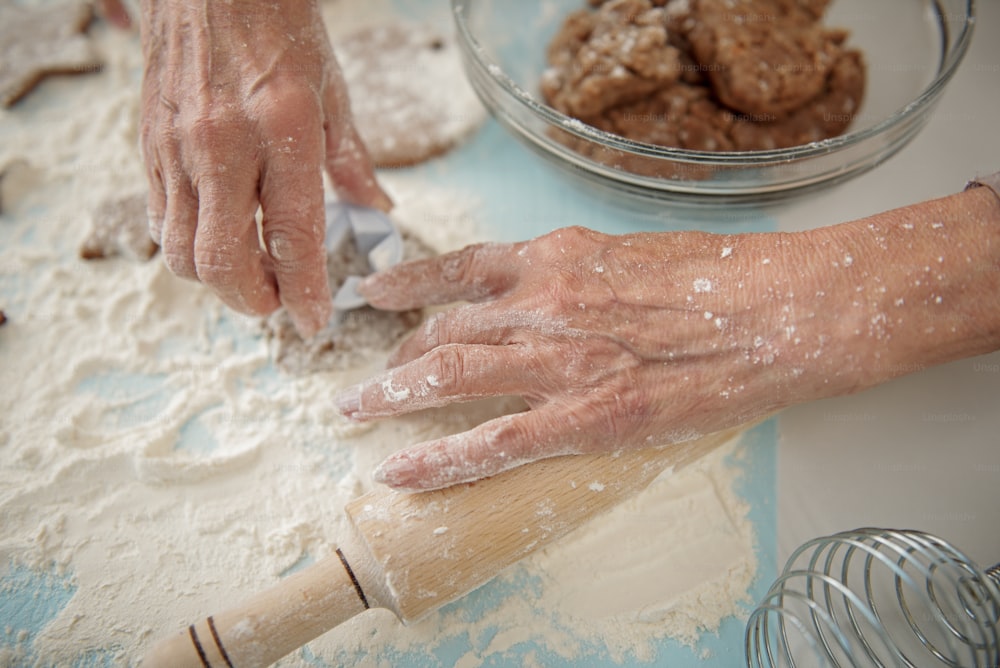 Top view close up of hands of old woman making shape of star from dough. Focus on flour and rolling pin