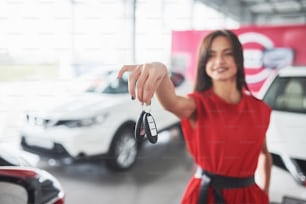 Lächelnder Autoverkäufer bei der Übergabe Ihrer neuen Autoschlüssel, Ihres Autohauses und Ihres Verkaufskonzepts. Glückliches Mädchen der Käufer.