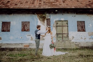 Beautiful young bride and groom outside in front of an old shabby house.