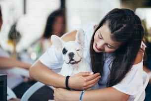 愛らしいフレンチブルドッグの子犬と一緒にカフェに座っている美しい若い女性。春または夏の屋外の街。犬をテーマにした人々。