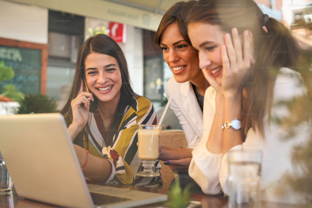 Tres mujeres jóvenes conversando en un café y usando una computadora portátil.