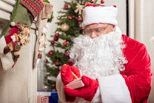 For obedient child. Portrait of concentrated Santa Claus signing gift box while standing near fireplace