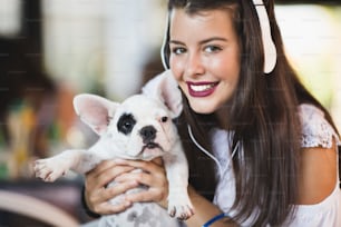 Schöne junge Frau sitzt im Café mit ihrem entzückenden französischen Bulldoggenwelpen. Frühlings- oder Sommerstadt im Freien. Menschen mit Hunden Thema.