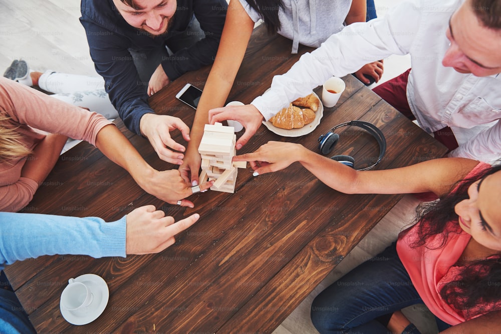 Vista dall'alto foto creativa di amici seduti al tavolo di legno. Amici che si divertono mentre giocano a un gioco da tavolo.