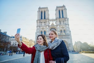 Zwei junge Mädchen spazieren zusammen in Paris und machen Selfies mit dem Handy in der Nähe der Kathedrale Notre-Dame. Tourismus- oder Freundschaftskonzept