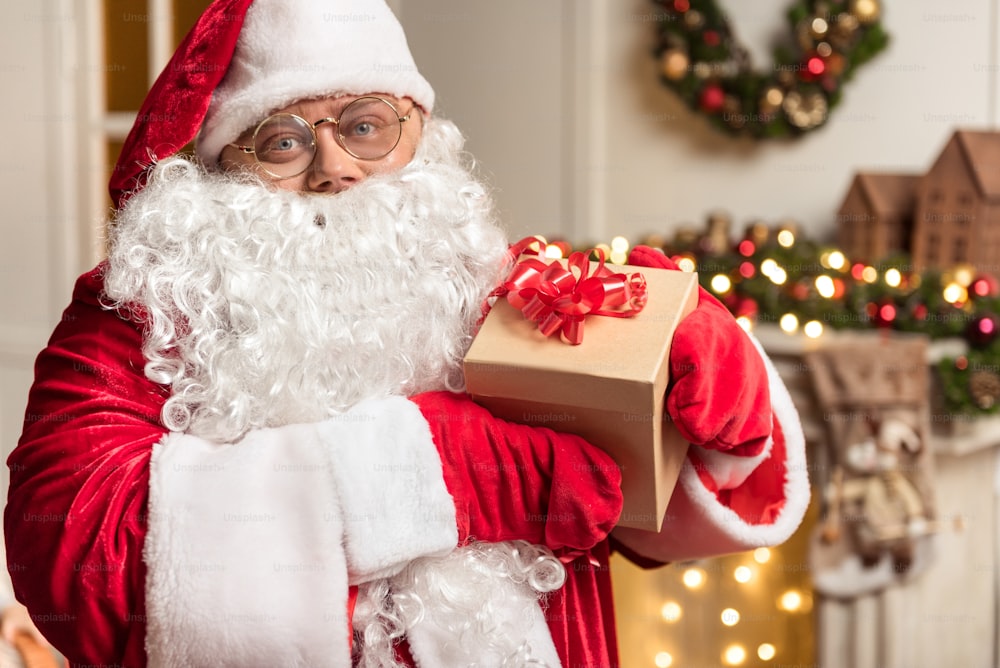 Merry Christmas. Portrait of kind Father Frost showing present box and smiling. He is wearing red and white costume