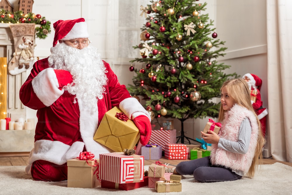 Give me one more present. Cute female child is looking at Santa Claus with hope. Fat man is sitting on floor and gesturing surprisingly