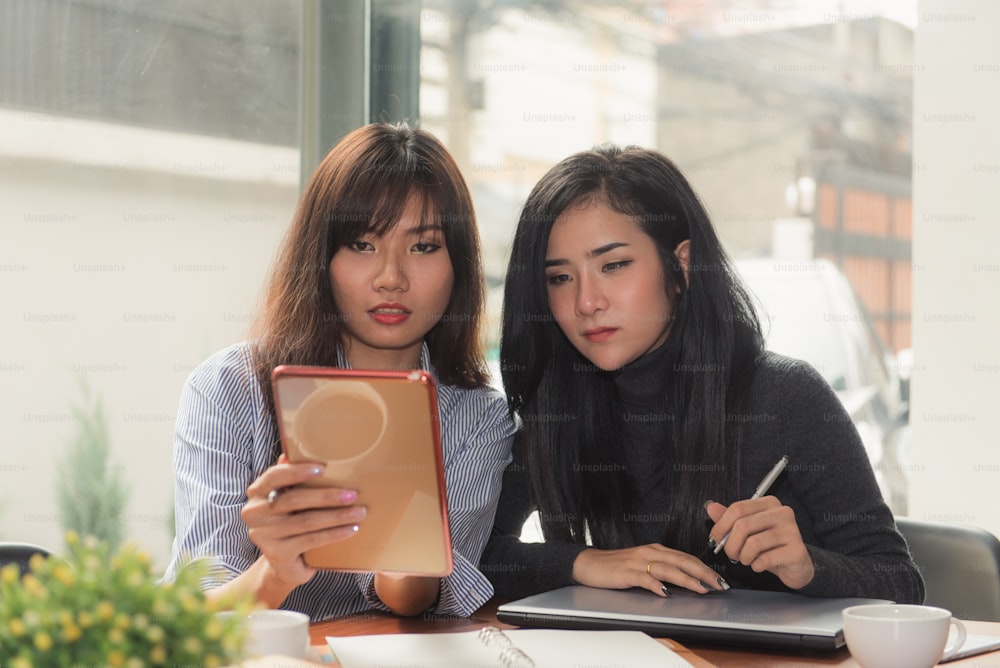 One-on-one meeting.Two young business women sitting at table in cafe. Girl shows colleague information on laptop screen. Girl using smartphone blogging. Teamwork business meeting. Freelancers working.
