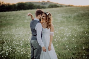 Beautiful young bride and groom outside in green nature at romantic sunset.
