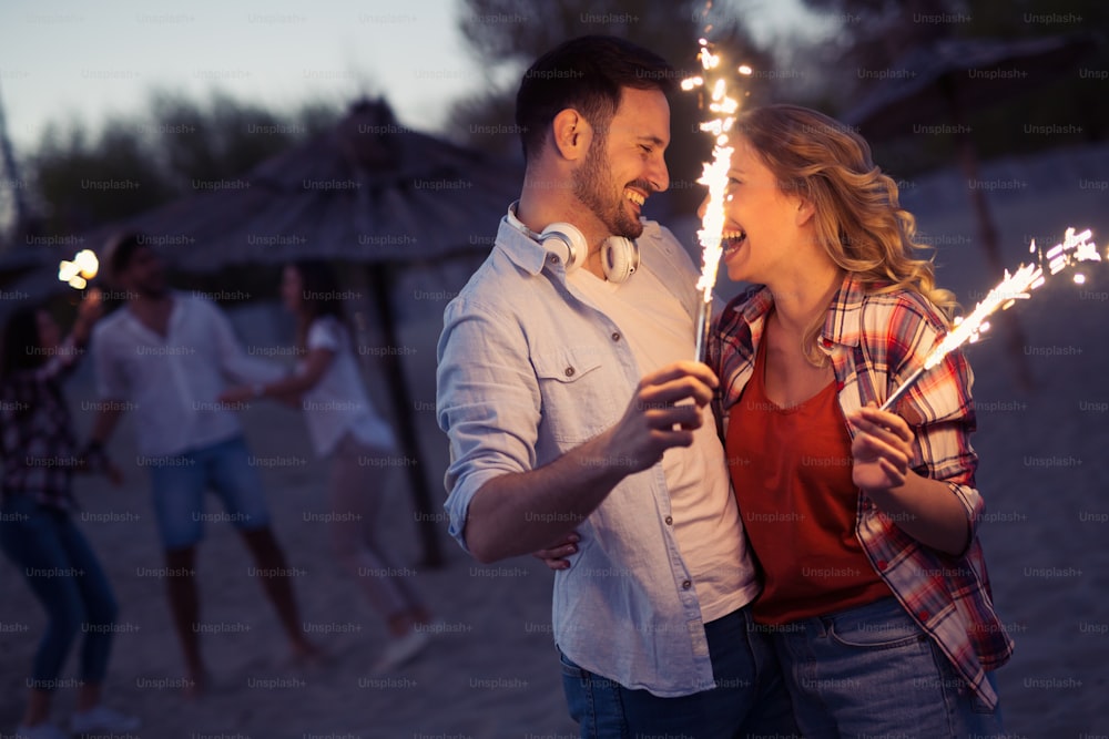 Happy group of friends lighting sparklers and enjoying freedom at beach during sunset