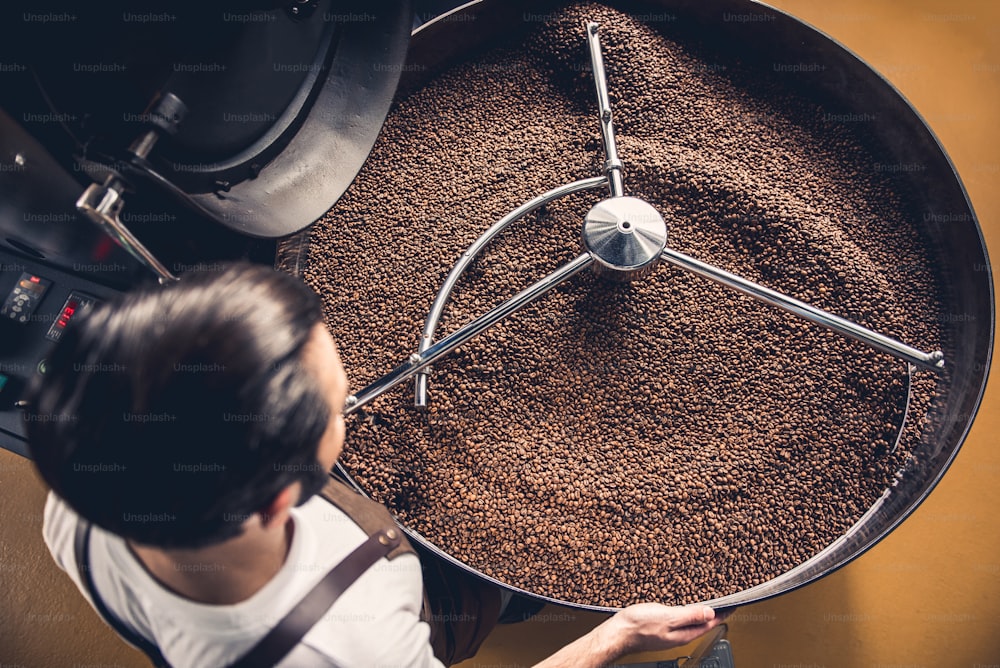 Top view coffee roaster worker controlling beans falling into spinning cooler professional machine. Arabica concept