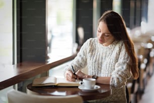 Beautiful young woman sitting in restaurant and writing