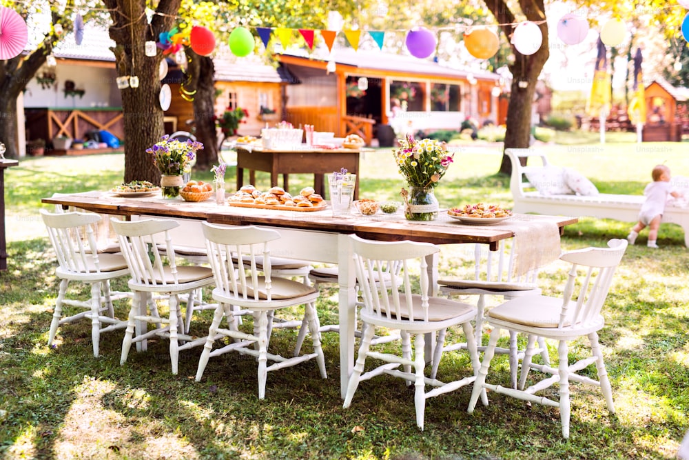 야외 정원 파티 또는 축하를위한 테이블 세트. 정원의 장식 된 테이블에 꽃과 달콤하고 짭짤한 간식.
