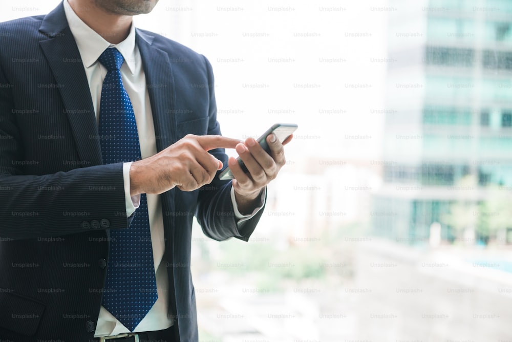 Businessman using mobile phone app texting outside of office in urban city with skyscrapers buildings in the background. Young asian man holding smartphone for business work.