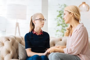 My family. Sad unhappy smart girl looking at her mother and holding her hands while sitting together with her