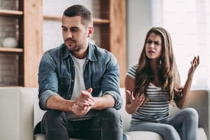 Upset couple at home. Handsome man and beautiful young woman are having quarrel. Sitting on sofa together. Family problems.