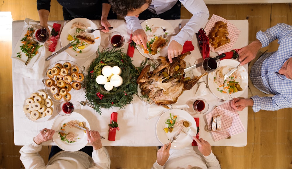 Grande família irreconhecível sentada à mesa, comendo, celebrando o Natal juntos em casa. Visão de alto ângulo.