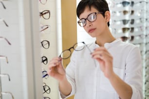 건강 관리, 시력 및 시력 개념 - 광학 매장에서 안경을 선택하는 행복 한 아름 다운 여자